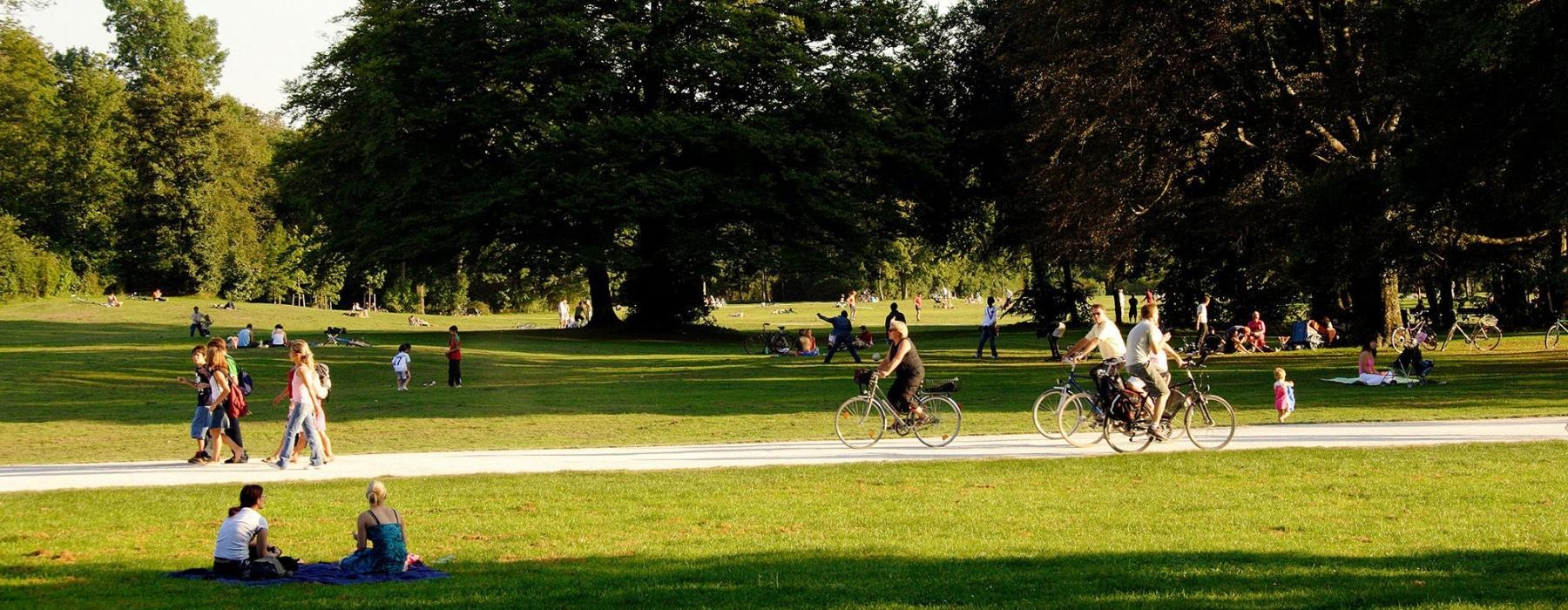 A park with many people riding bikes, having a picnic, and walking.